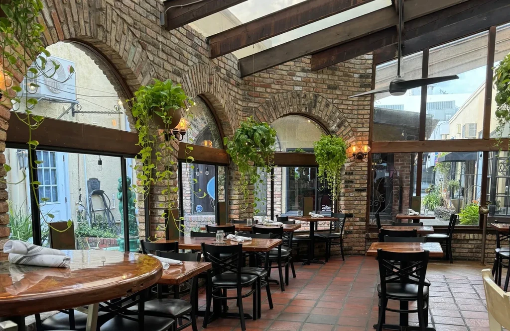 Naturally lit restaurant interior with brick arches and abundant hanging plants.