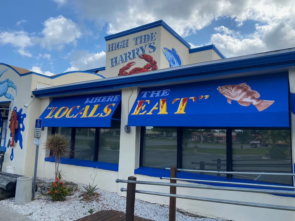 Facade of High Tide Harry's restaurant, beige with marine murals and blue awnings.