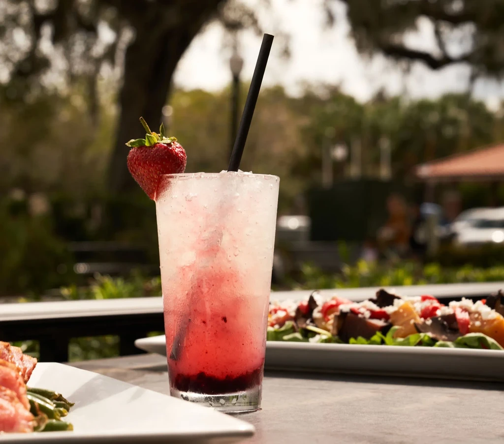 Layered red iced drink with strawberry and straw on an outdoor table.