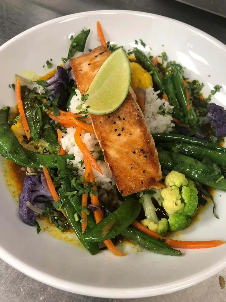 Close-up of pan-seared salmon, rice, colorful vegetables, and sauce.