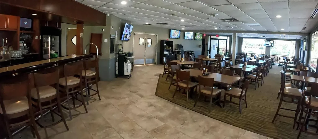 Casual restaurant interior with bar, dining tables, and wall-mounted TVs.
