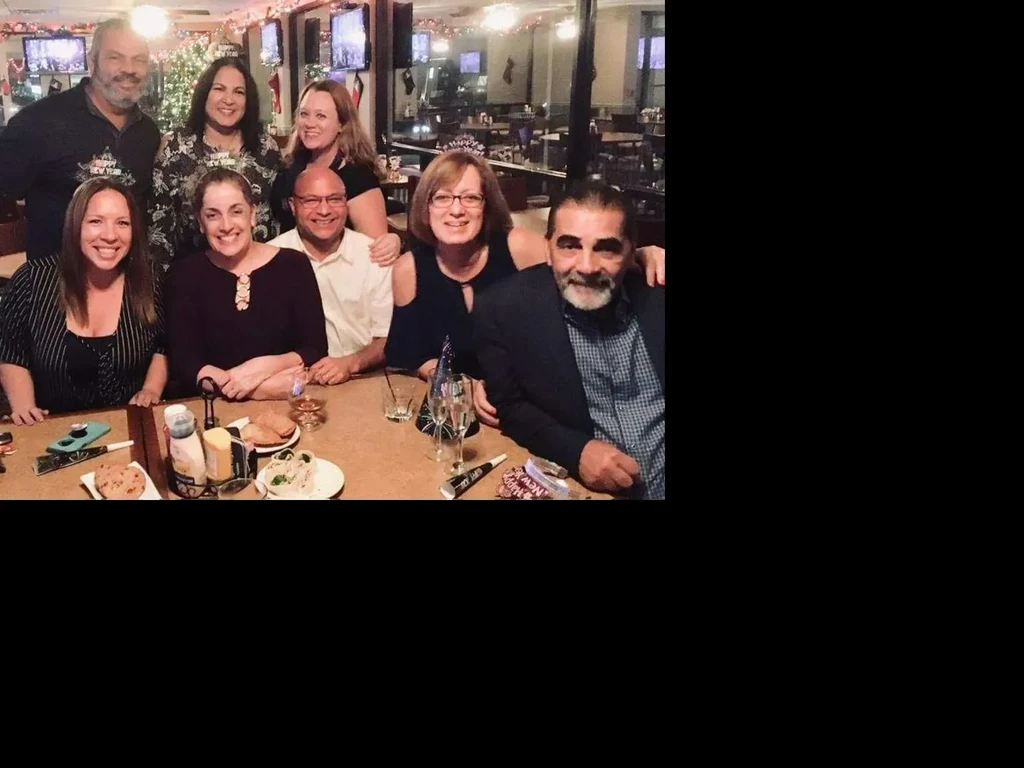 Eight smiling adults celebrating New Year's around a restaurant table.