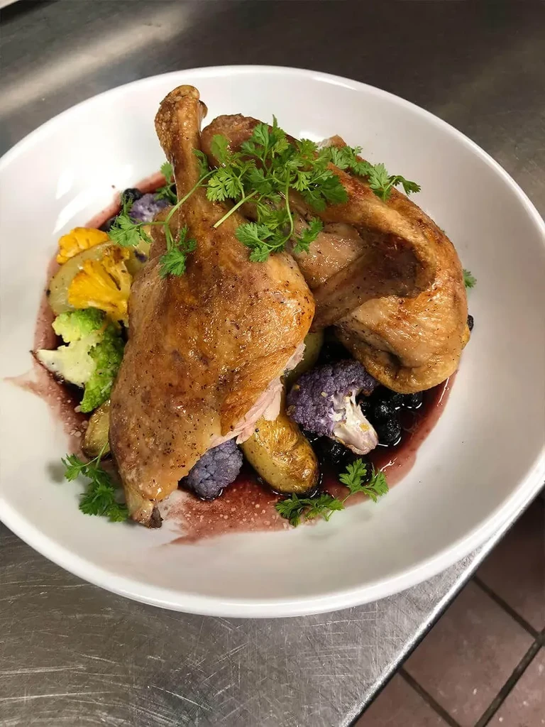 Crispy roasted poultry legs with colorful vegetables, sauce, and berries.