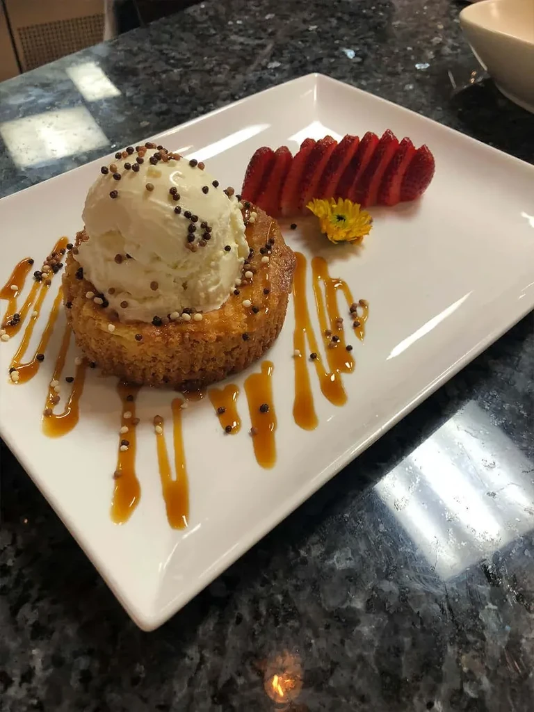 Plated golden-brown cake with ice cream, sprinkles, strawberries, and caramel sauce.