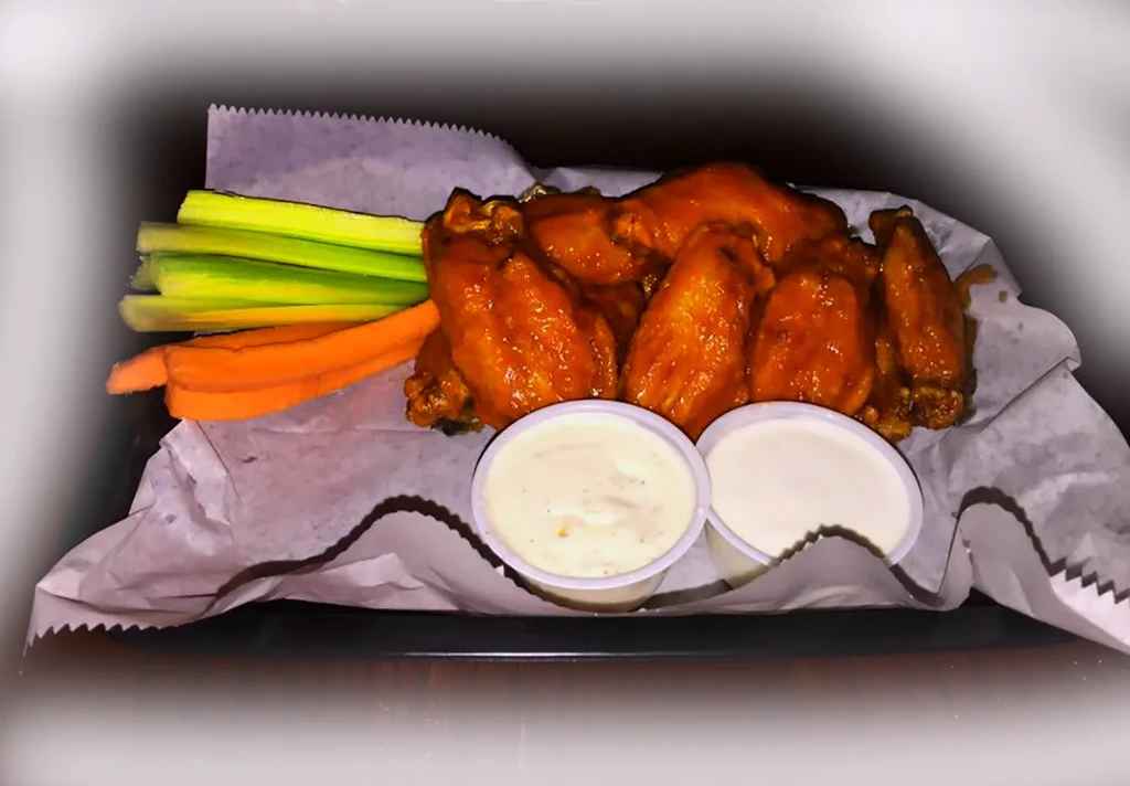 Orange-red buffalo chicken wings with celery, carrots, and dipping sauces.