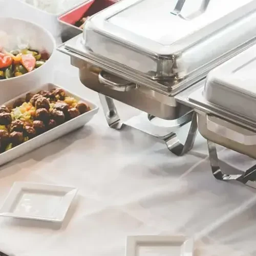 Buffet table with silver chafing dishes, meatballs, salad, and empty plates.