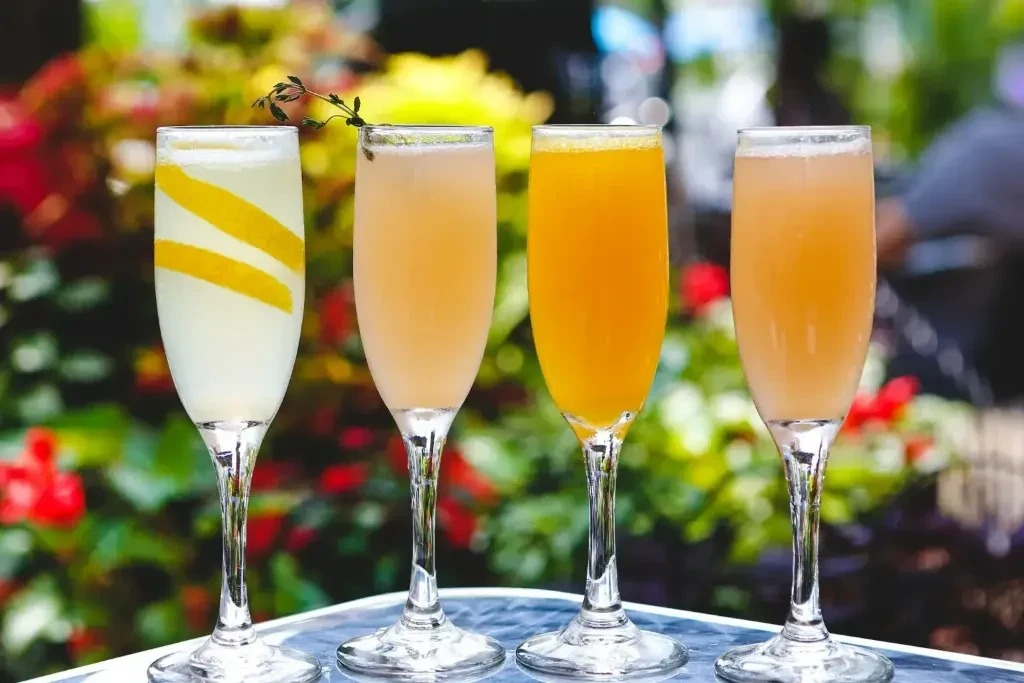 Four fluted glasses with colorful cocktails and garnishes on a patio.