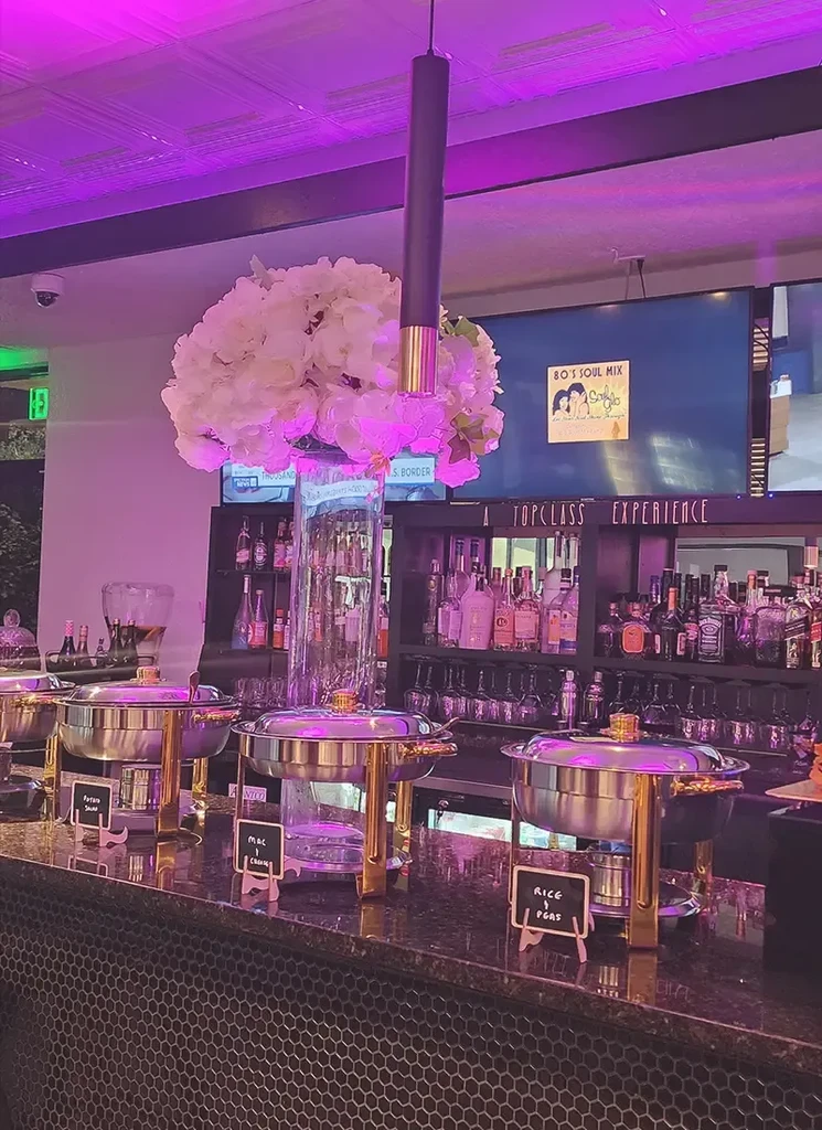 Purple-lit restaurant buffet with food, flowers, and a stocked bar.