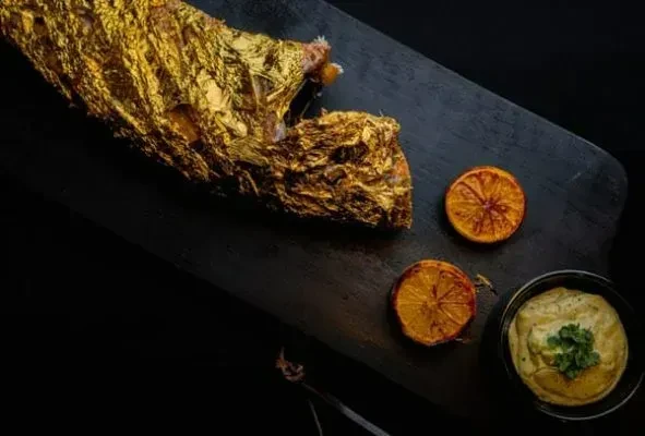 Gilded meat with caramelized citrus and herb dip on a dark board.