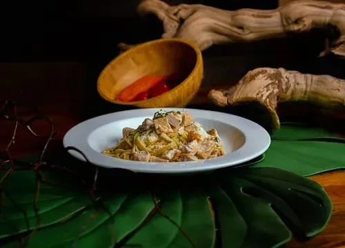 Creamy pasta with cubed chicken or fish, herbs, green leaf placemat.