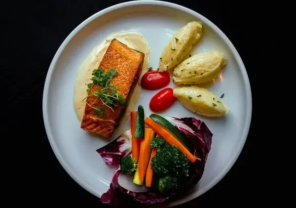 Pan-seared salmon, vegetables, and quenelles, finely plated on a white dish.