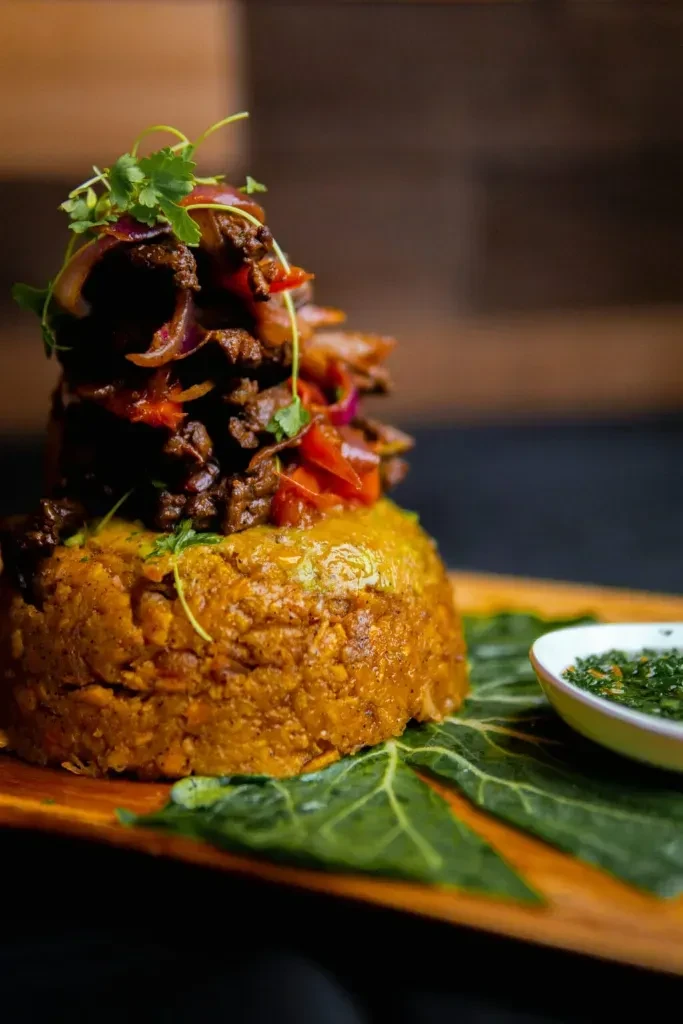 Cylindrical plantain mound with stewed meat, onions, cilantro, and green sauce.