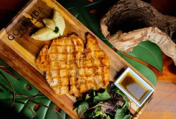 Grilled chicken, mashed potatoes, salad, sauce on 'GOZUMBA' wooden board.