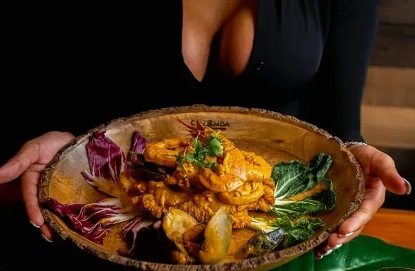 Rustic wooden bowl of shrimp and seafood in red sauce, garnished.