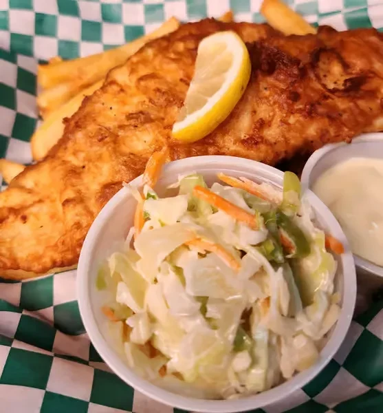 Golden battered fish and chips with lemon, coleslaw, and dipping sauce.