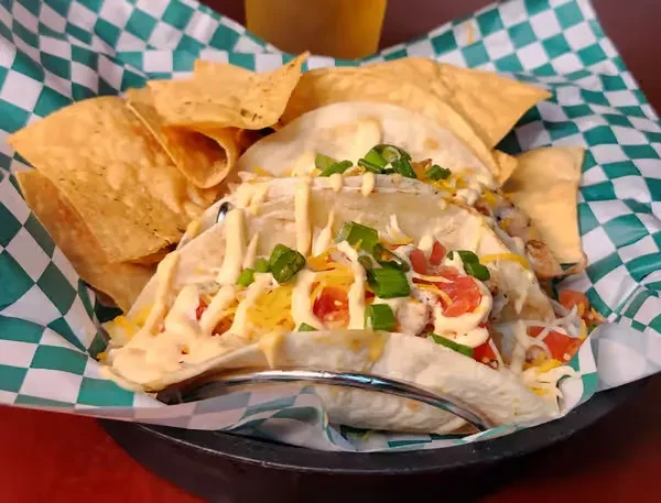 Two loaded soft-shell tacos and chips in a checkered basket.