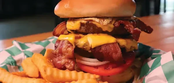 Stacked double burger with bacon, cheese, and crinkle fries in a basket.