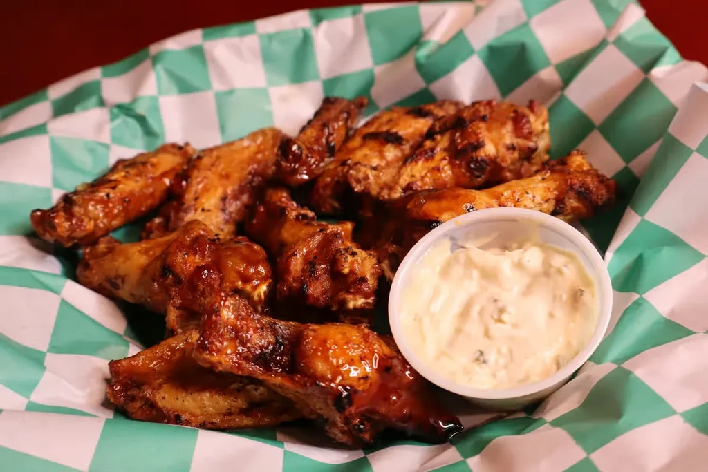 Generously sauced chicken wings and creamy dip in a checkered basket.
