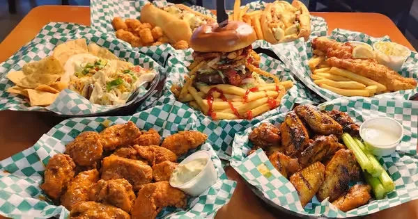 Overhead view: tall burger, wings, fish, and nachos on a casual table.