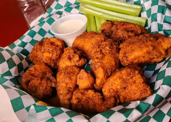 Crispy fried chicken wings in a checkered basket with sauce and celery.