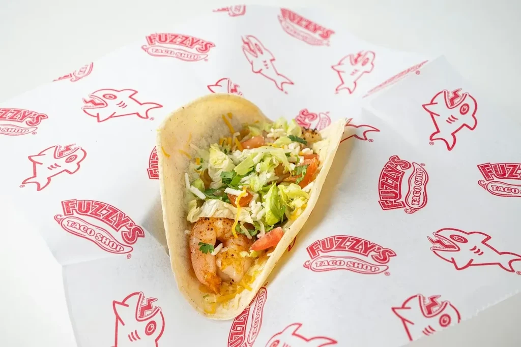 Single shrimp taco with fresh toppings on Fuzzy's Taco Shop branded paper.
