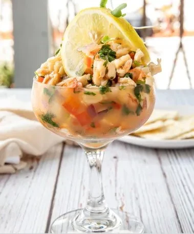 Close-up of colorful shrimp ceviche cocktail in a glass, garnished with lemon.