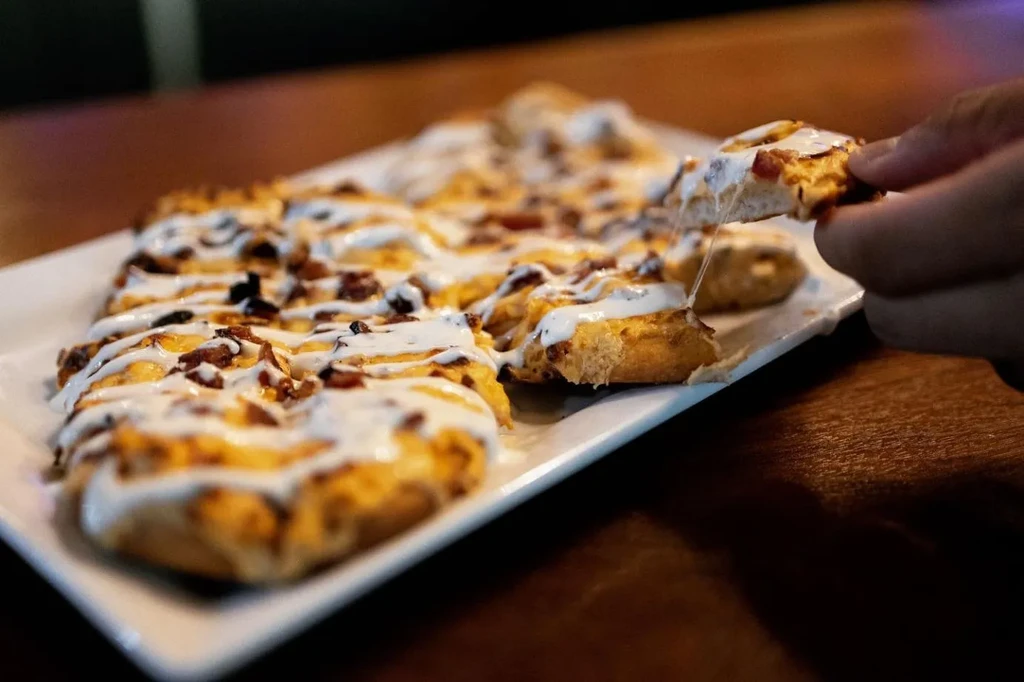 Hand pulls a cheesy bacon flatbread piece with stretching cheese.