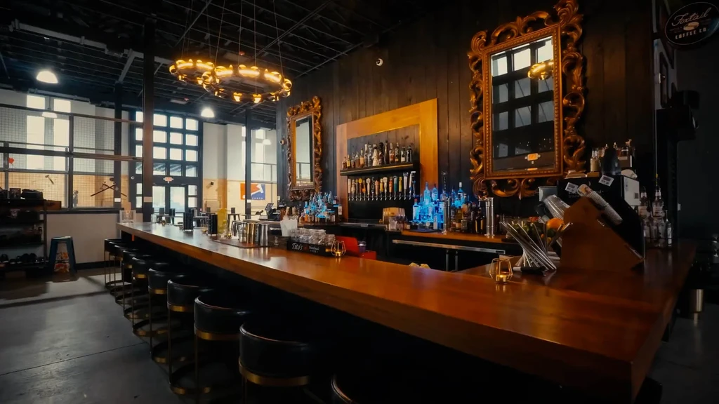 Well-stocked industrial bar with dark wooden counter and gold chandelier.