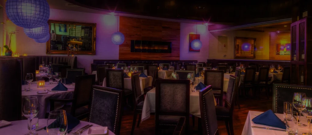 Dimly lit, upscale restaurant dining room with purple lighting and candles.