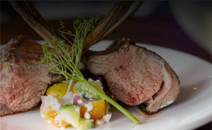Seared medium-rare lamb chops with colorful diced salad and herbs.