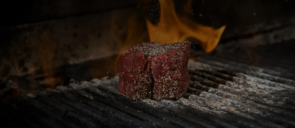 Heavily seasoned raw meat grilling over bright orange flames.