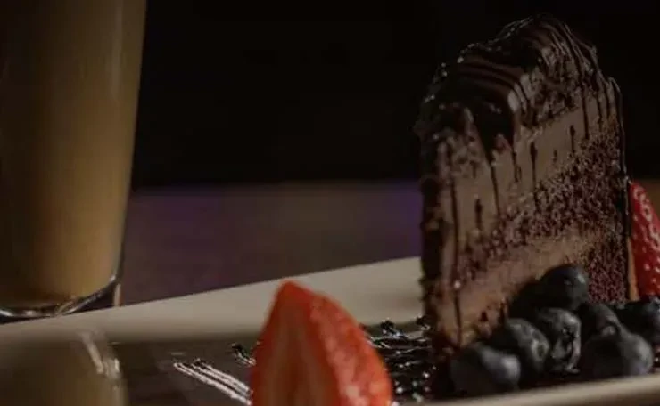 Slice of frosted chocolate cake with fresh berries and chocolate drizzle.