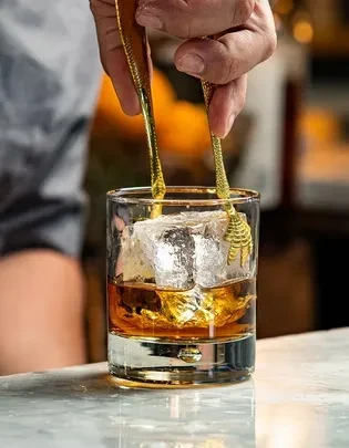 Hand uses unique golden talon tongs to adjust whiskey ice.