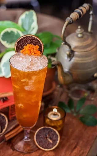 Orange cocktail garnished with dried orange and flower, on wooden surface.