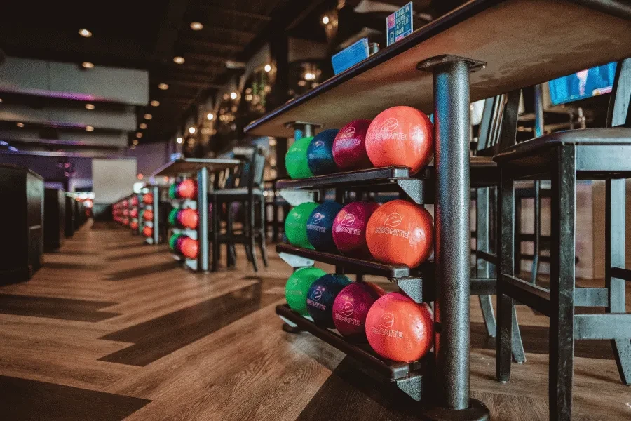 Brightly colored bowling balls on racks in a modern bowling alley bar.