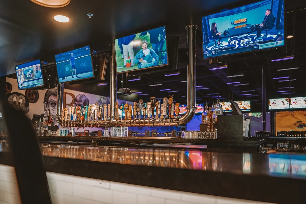 Modern sports bar: long bar, many beer taps, multiple flat-screen TVs.