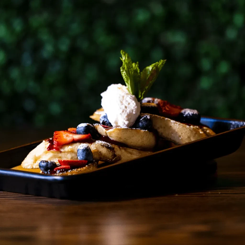 Plated French toast with berries, whipped cream, mint, powdered sugar.