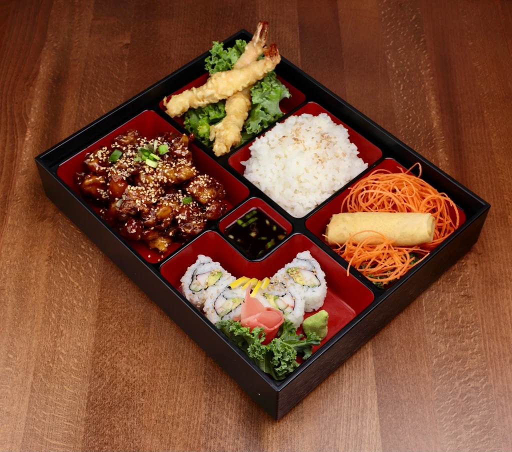 Black bento box with sushi, tempura, chicken, rice, and spring roll.