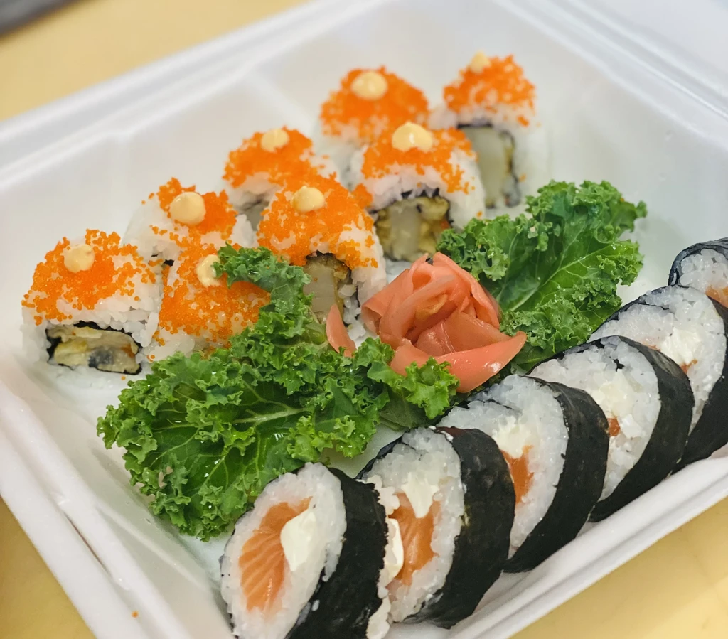 California and salmon sushi rolls with ginger and lettuce in a takeout container.