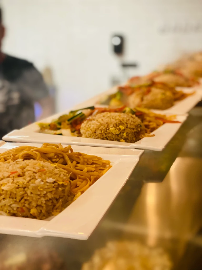 Restaurant serving line with plates of fried rice, noodles, and vegetables.