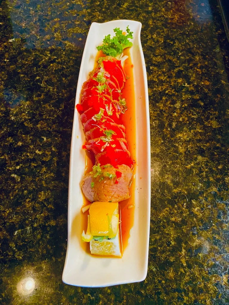 Long white plate featuring tuna sashimi, seared meat, and citrus roll.