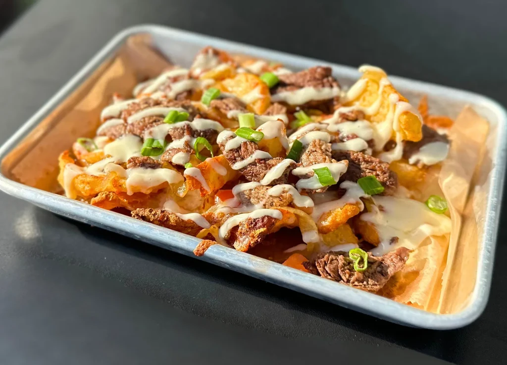 Loaded fries with meat, white sauce, and green onions in a tray.