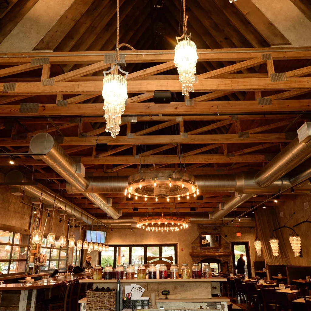 Rustic-industrial restaurant interior with exposed beams, unique chandeliers, and a bar.