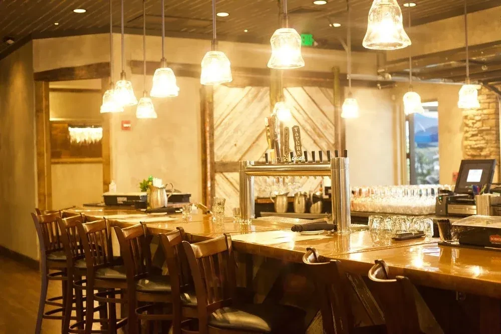 Rustic bar interior, wooden counter, beer taps, pendant lights, outdoor view.