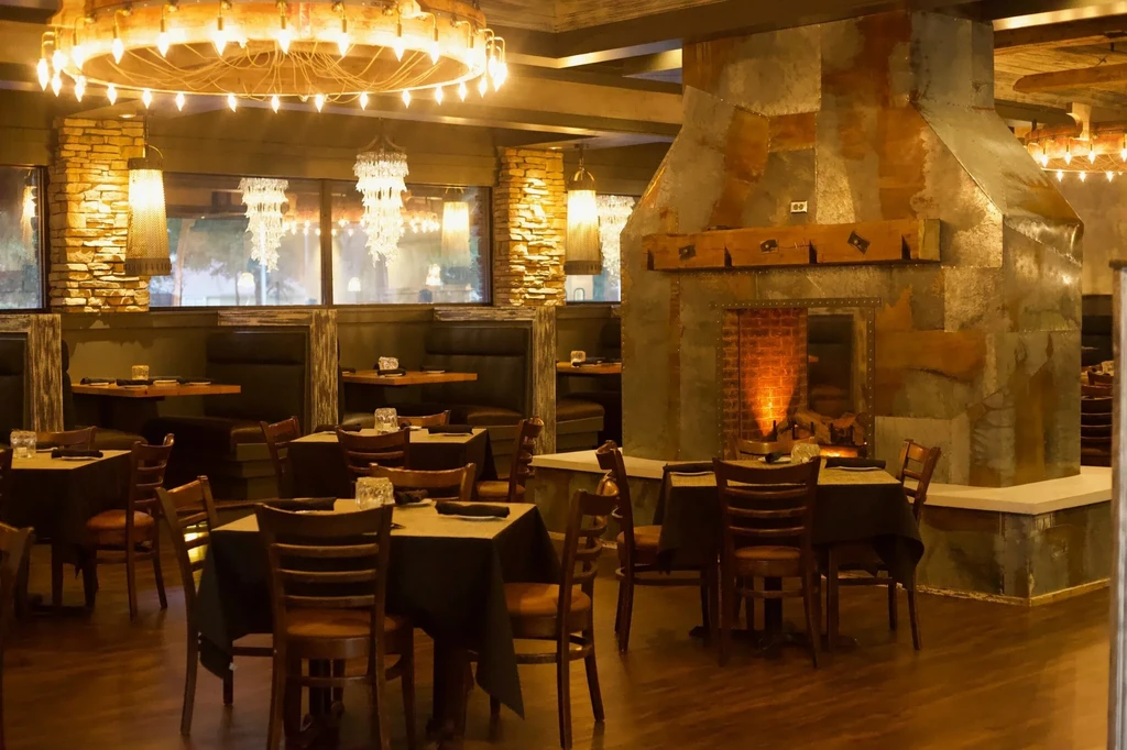 Upscale restaurant dining area with rustic metal fireplace and warm lighting.