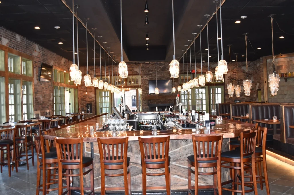 Modern industrial bar with large central bar, brick walls, unique lights.