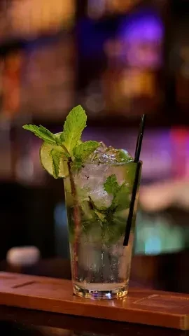 Mojito cocktail with mint, lime, and ice on a wooden bar.