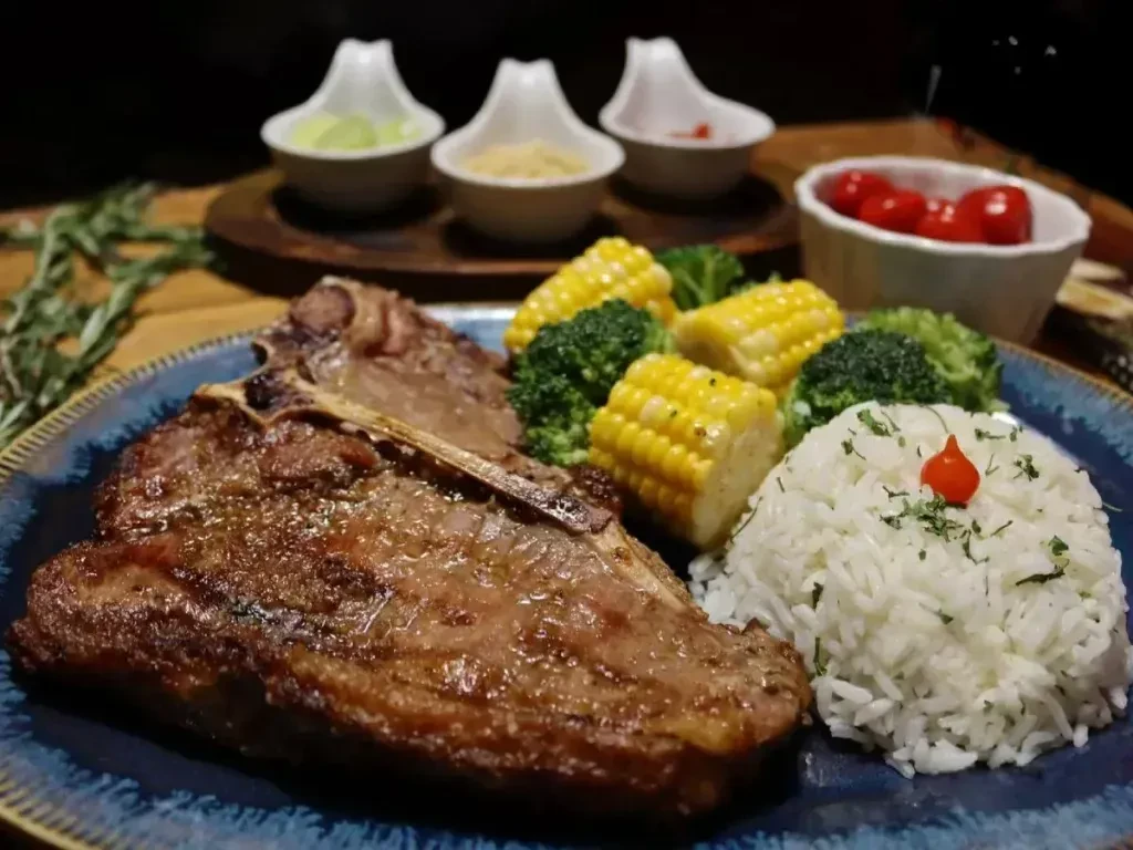 A T-bone steak, rice, corn, and broccoli on a blue plate.
