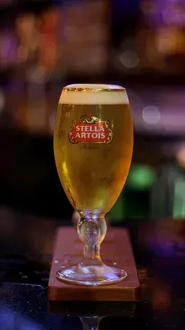 A cold Stella Artois beer chalice with foam on a bar.