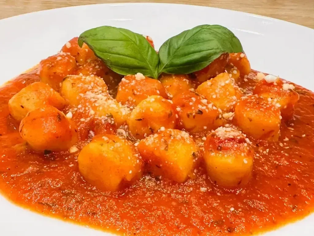 Plate of golden gnocchi with red tomato sauce, cheese, and basil.
